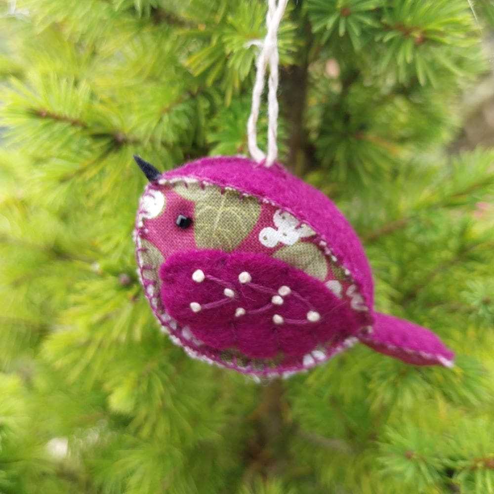 a hand stitched felt and fabric bird decoration, the felt is purple and the fabric is green, purple with pearly snowberries