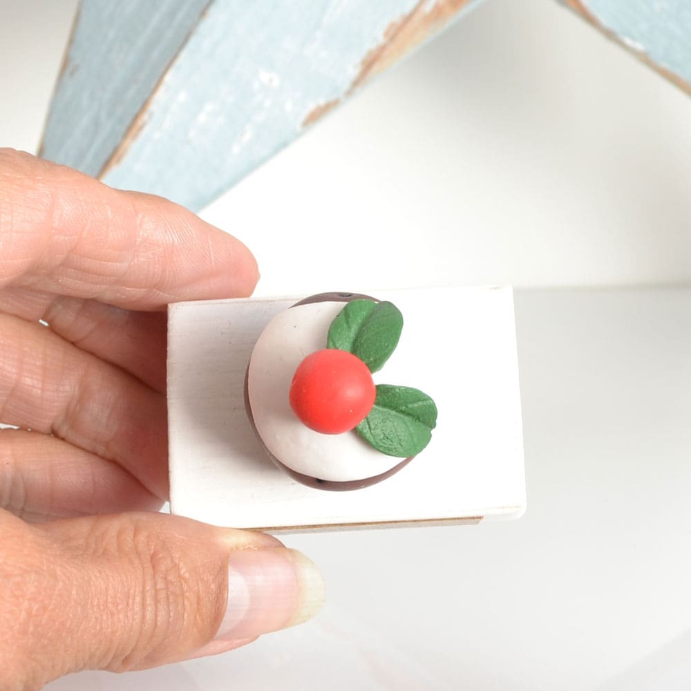 Clay Christmas Pudding ornament set on a white wooden base with the pun 'A Jolly Pud Christmas.