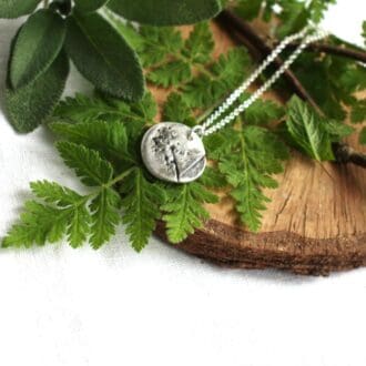 Solid silver circular pendant with imprint of the herb sweet cicily, displayed on fronds of sweet cicily