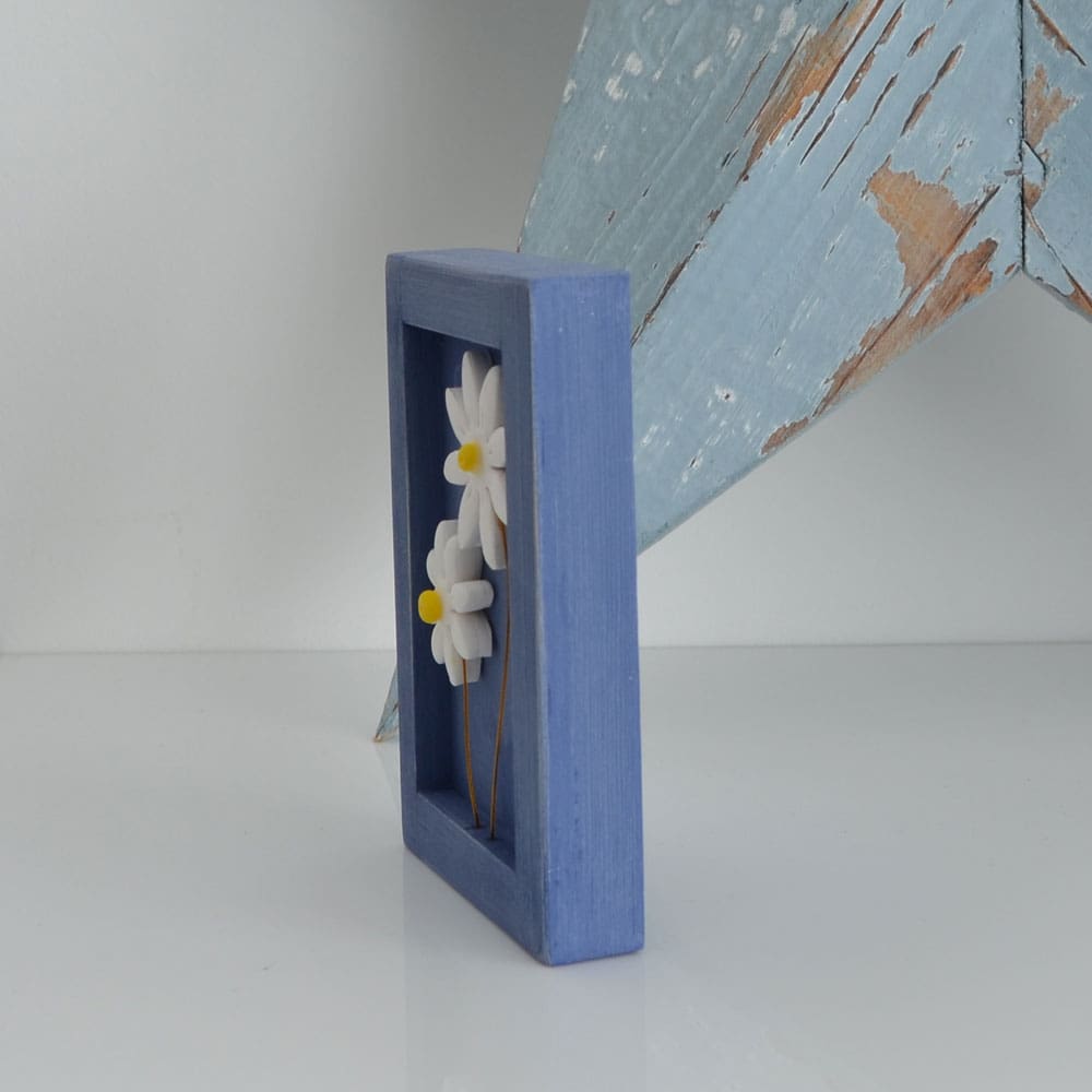 Miniature handmade wooden open frame in a distressed blue chalk paint with two small clay daisy flowers