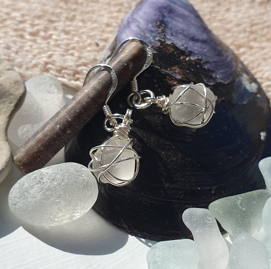 White sea glass nuggets wrapped in silver wire pair of dangly earrings displayed on a large mussel shell