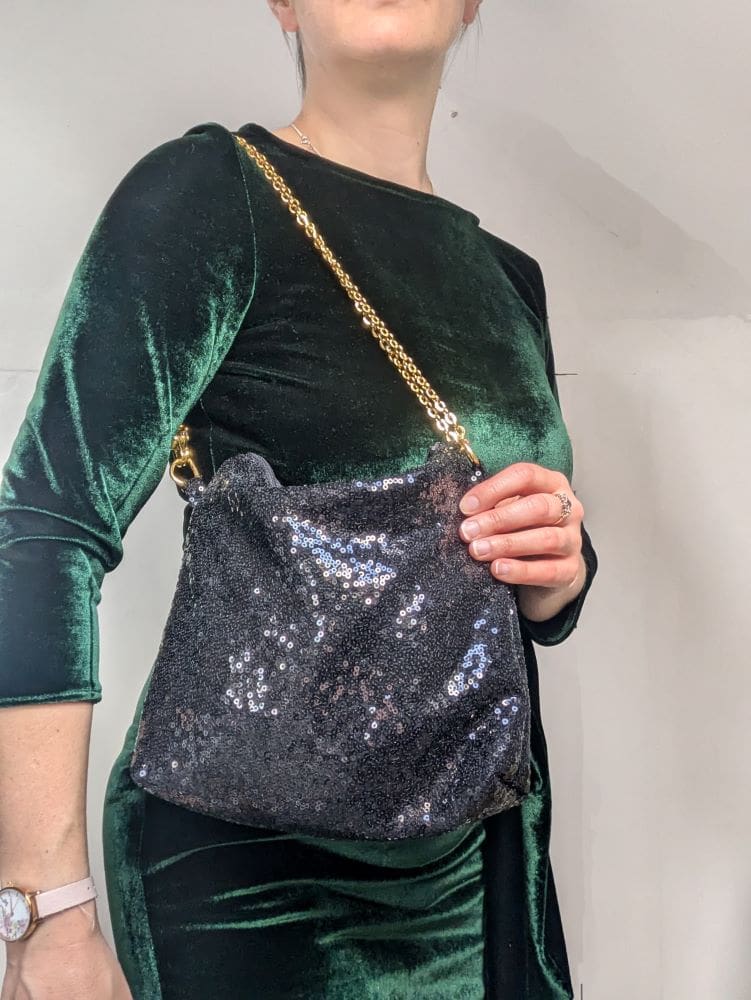 Black sequin evening bag shown worn on a woman in a green dress