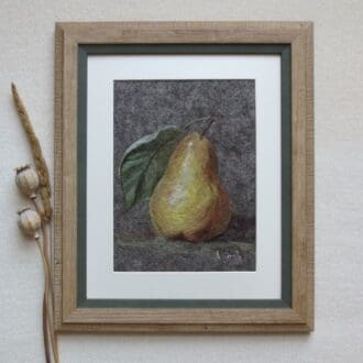 A wool felted picture of a gold coloured pear with a green leaf on a grey felt background. The picture has a cream mount and a pale wood frame with green inside edge.