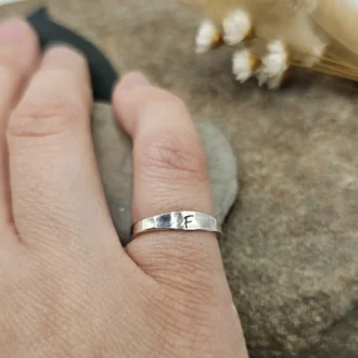 Handcrafted recycled sterling silver initial engraved ring displayed on jeweller's little finger of right hand