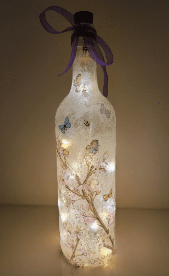 lit up Standard wine bottle with flower and butterfly design. Purple ribbon tied around the neck