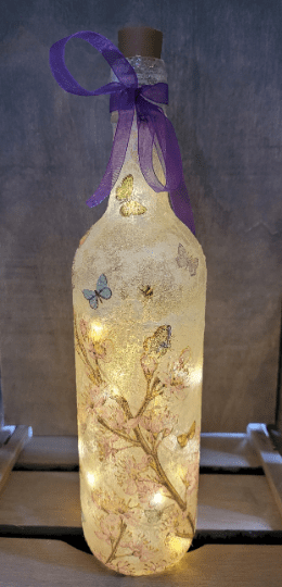 lit up standard wine bottle with flower butterfly design. Purple ribbon tied around the neck