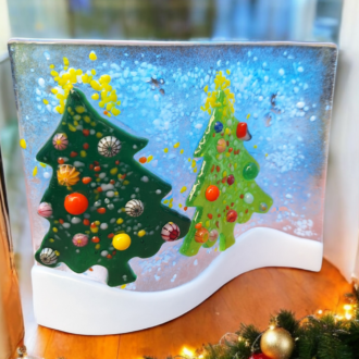 Handmade fused glass Christmas wave featuring two green Christmas trees with colourful ornaments, set against a snowy blue background. Freestanding home decor, perfect for adding festive charm to your living space or gifting as a unique Christmas decoration.