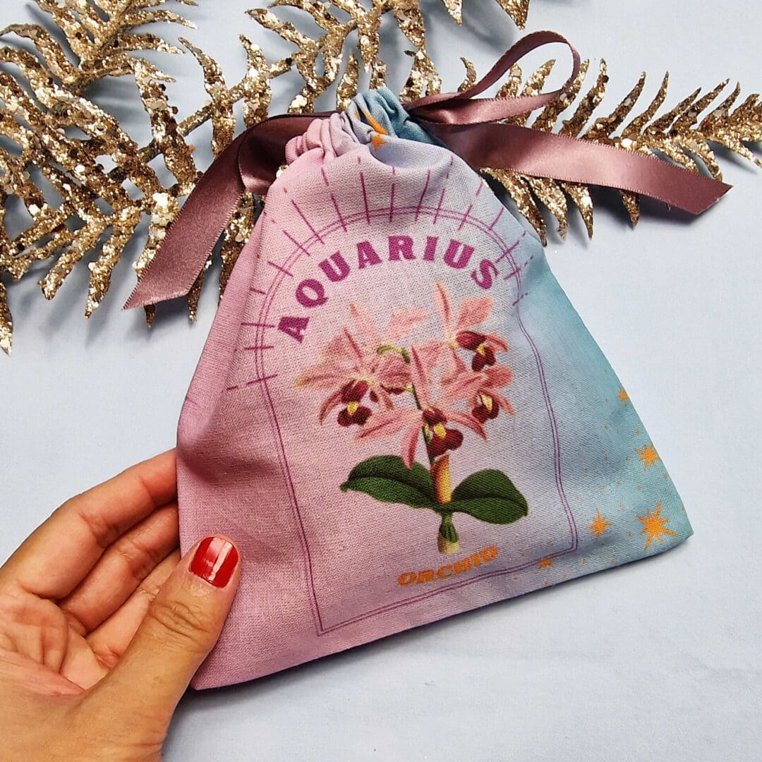 photo of a handmade cotton pouch with digital print of aquarius birth flower, orchid in purples and blues with eco-satin ribbon