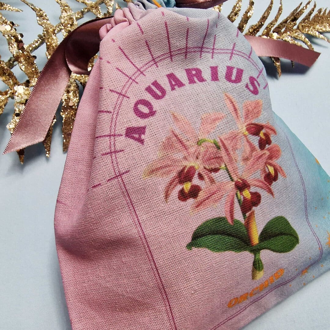 photo of a handmade cotton pouch with digital print of aquarius birth flower, orchid in purples and blues with eco-satin ribbon