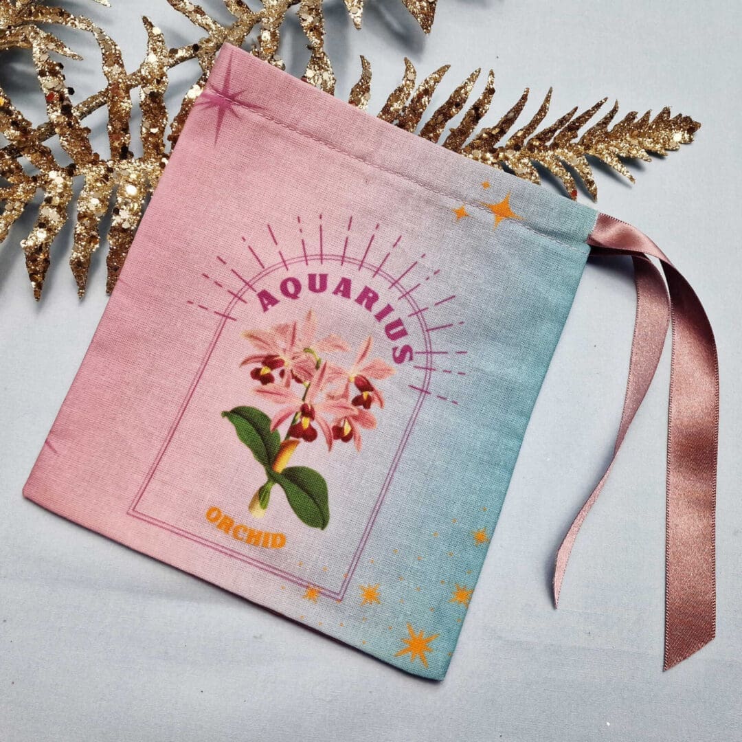 photo of a handmade cotton pouch with digital print of aquarius birth flower, orchid in purples and blues with eco-satin ribbon