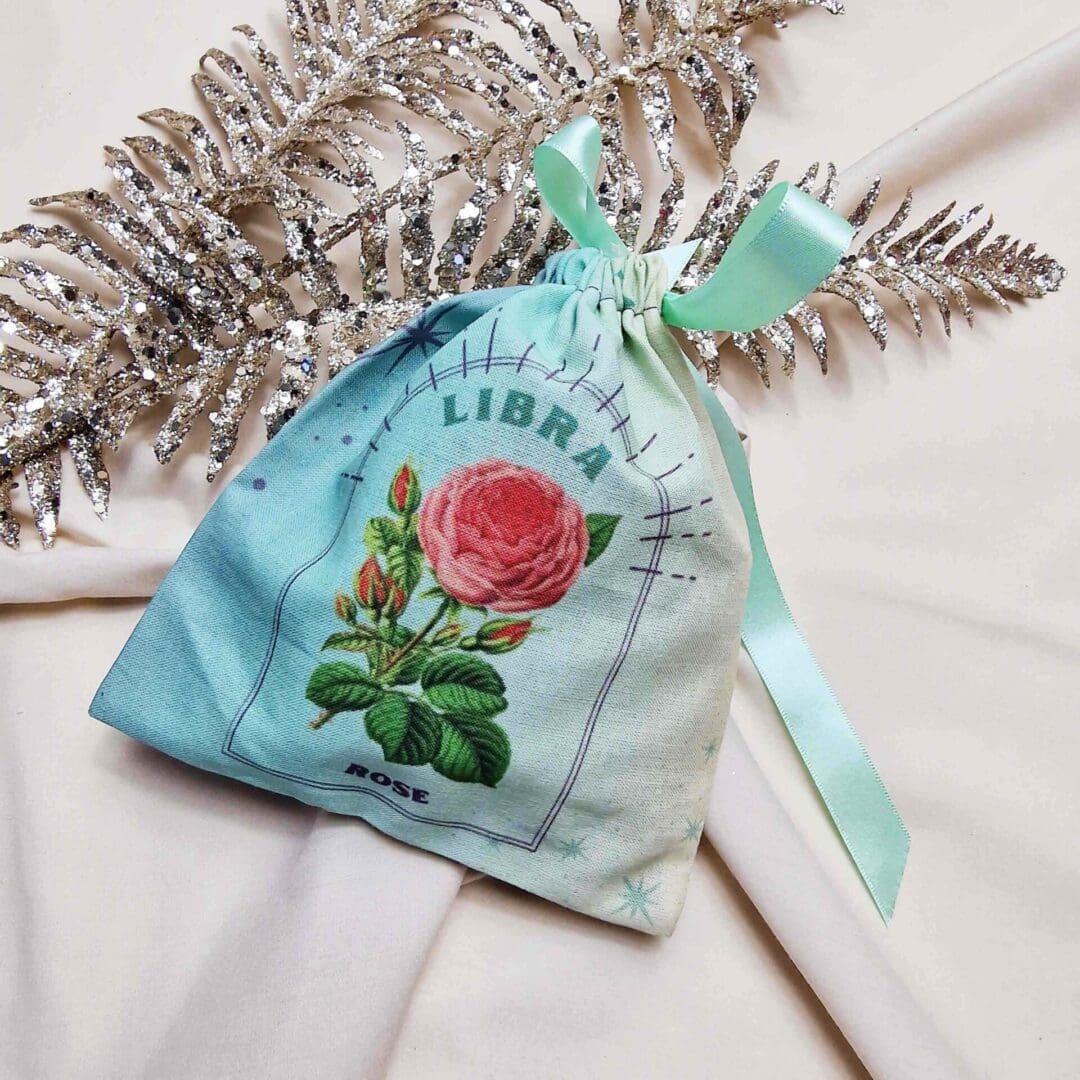 photo of a handmade cotton pouch with digital print of the libra birth flower, rose. finished with an eco-satin ribbon tie