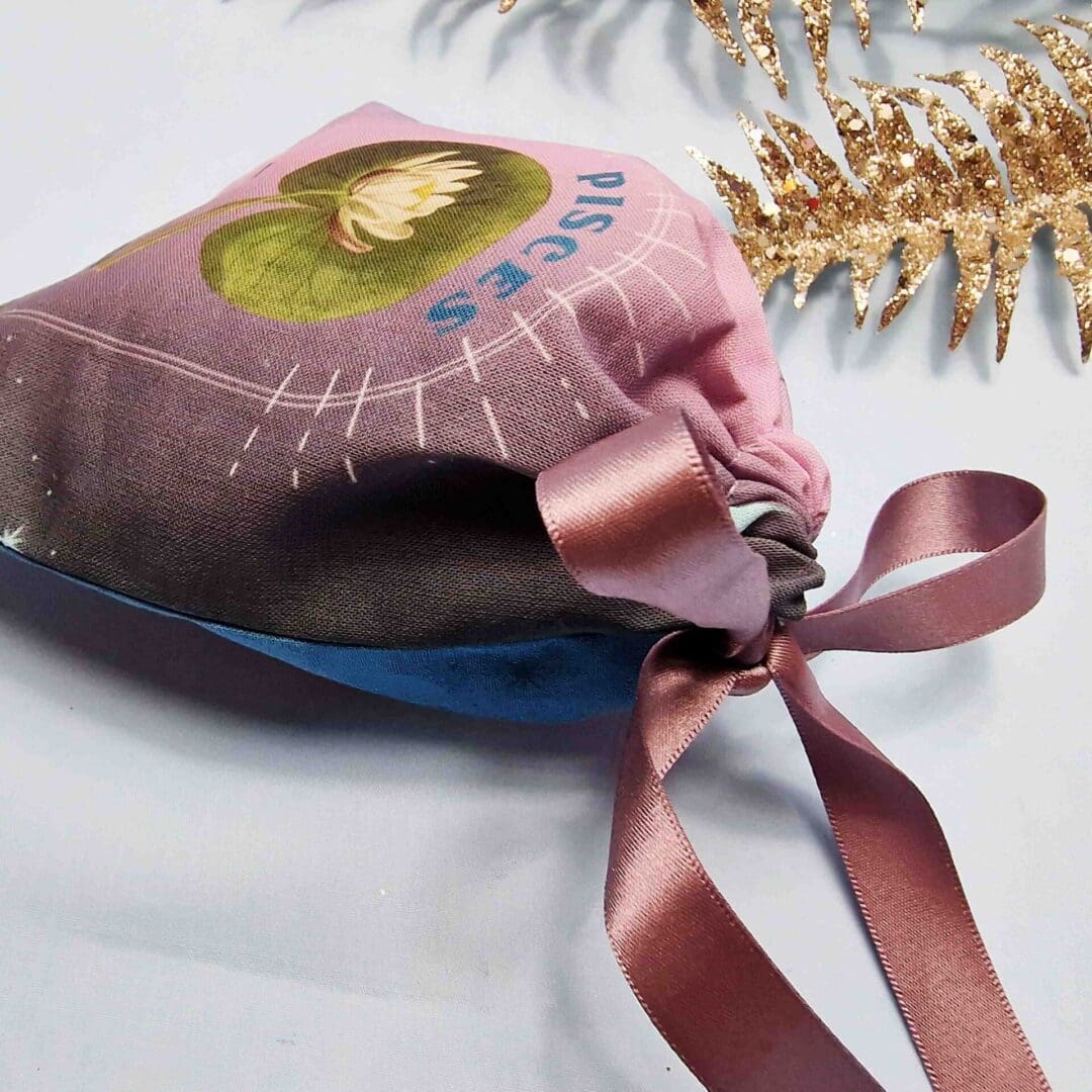 photo of a handmade cotton pouch with a digital print of the pisces birth flower, the water lily finished with an eco-satin mauve ribbon