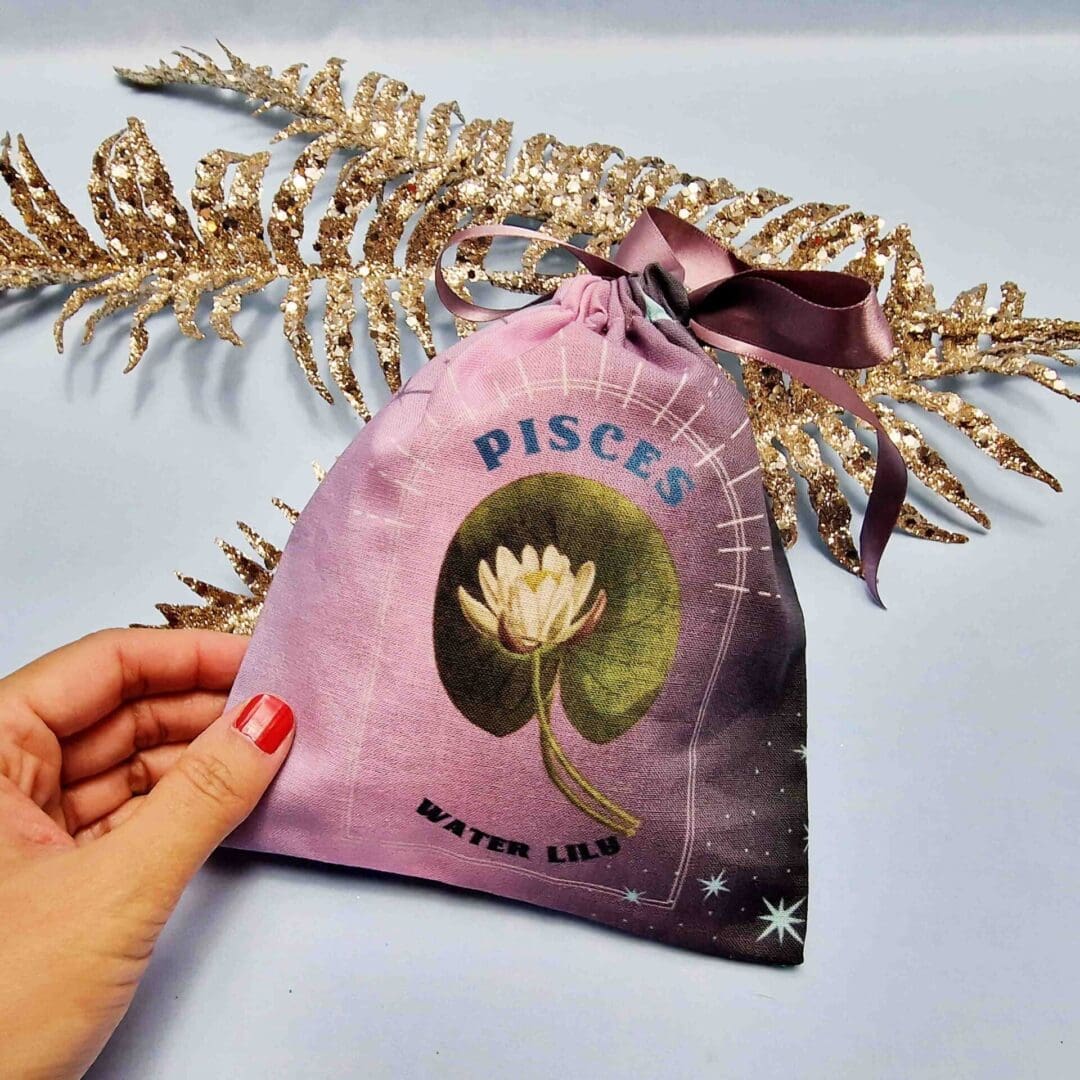 photo of a handmade cotton pouch with a digital print of the pisces birth flower, the water lily finished with an eco-satin mauve ribbon