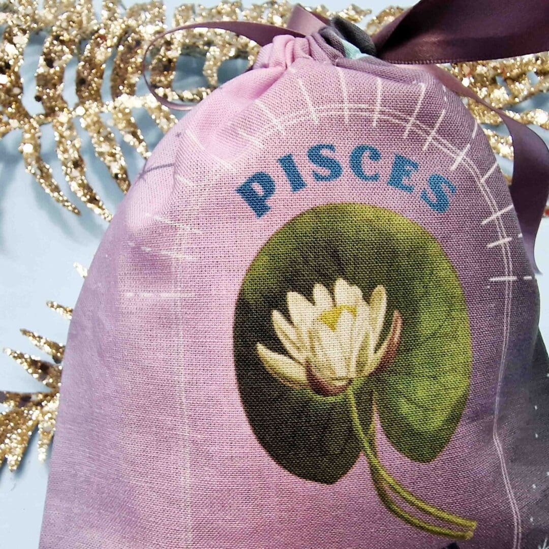 photo of a handmade cotton pouch with a digital print of the pisces birth flower, the water lily finished with an eco-satin mauve ribbon