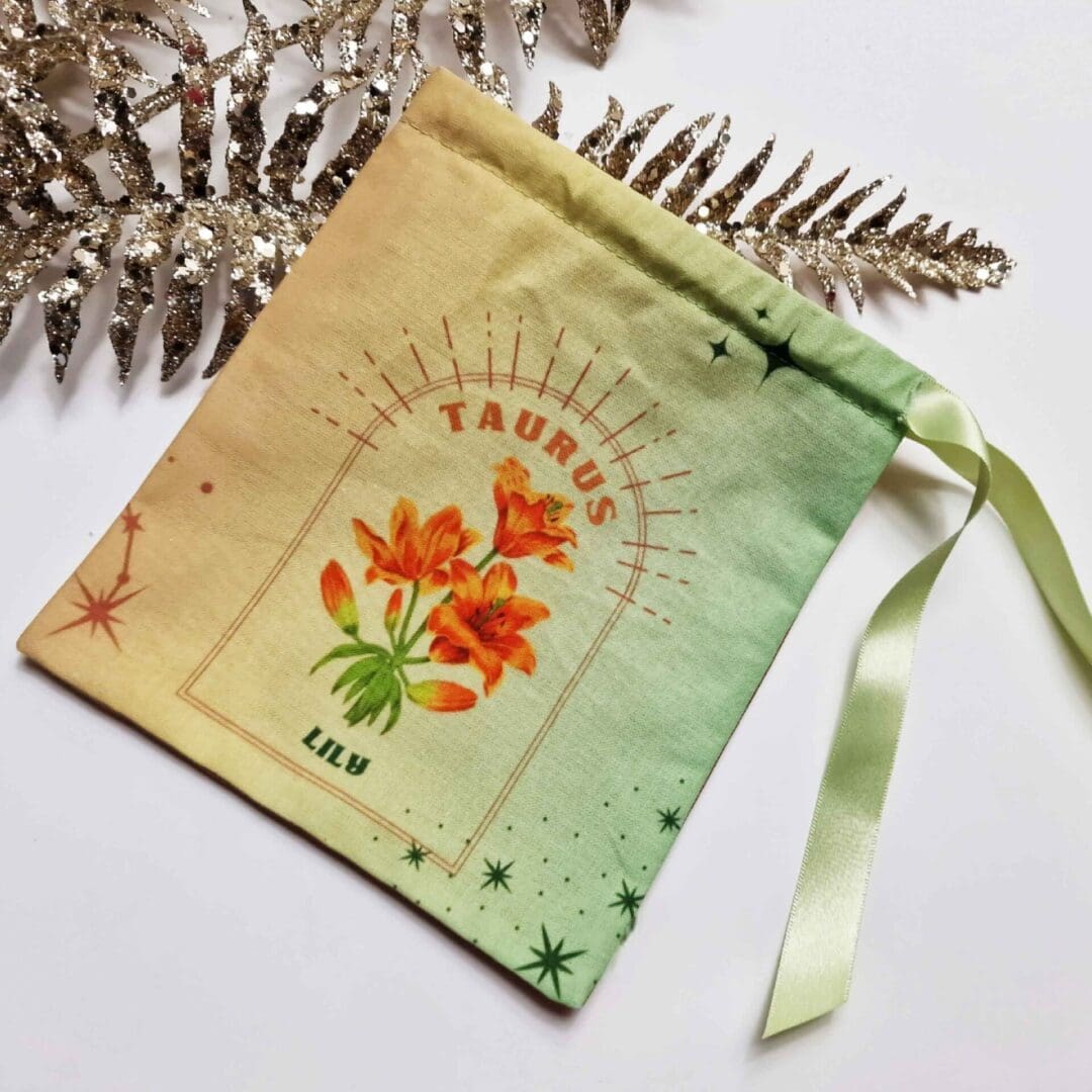 photo of a handmade cotton pouch featuring a digital print of the taurus birth flower, the orange lily, finished with eco-satin ribbon