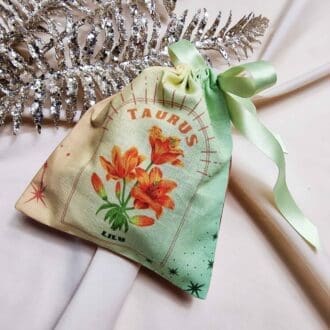 photo of a handmade cotton pouch featuring a digital print of the taurus birth flower, the orange lily, finished with eco-satin ribbon