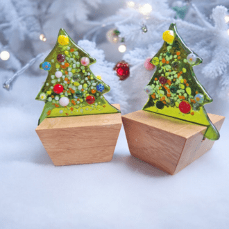 A pair of handmade fused glass Christmas trees set on wooden stands, featuring colourful decorative details. These mini Christmas tree ornaments are perfect as mantle piece decor, table top art, or holiday decorations. Ideal as a unique gift for mum, teacher gift, or festive glass ornament.