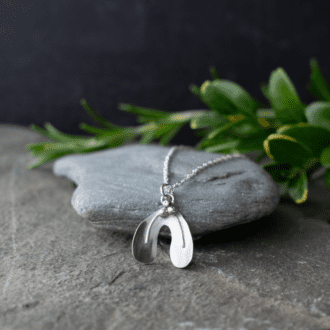 sterling silver necklace shaped like a mistletoe leaf with three berries. Pendant rests on slate with foliage in background