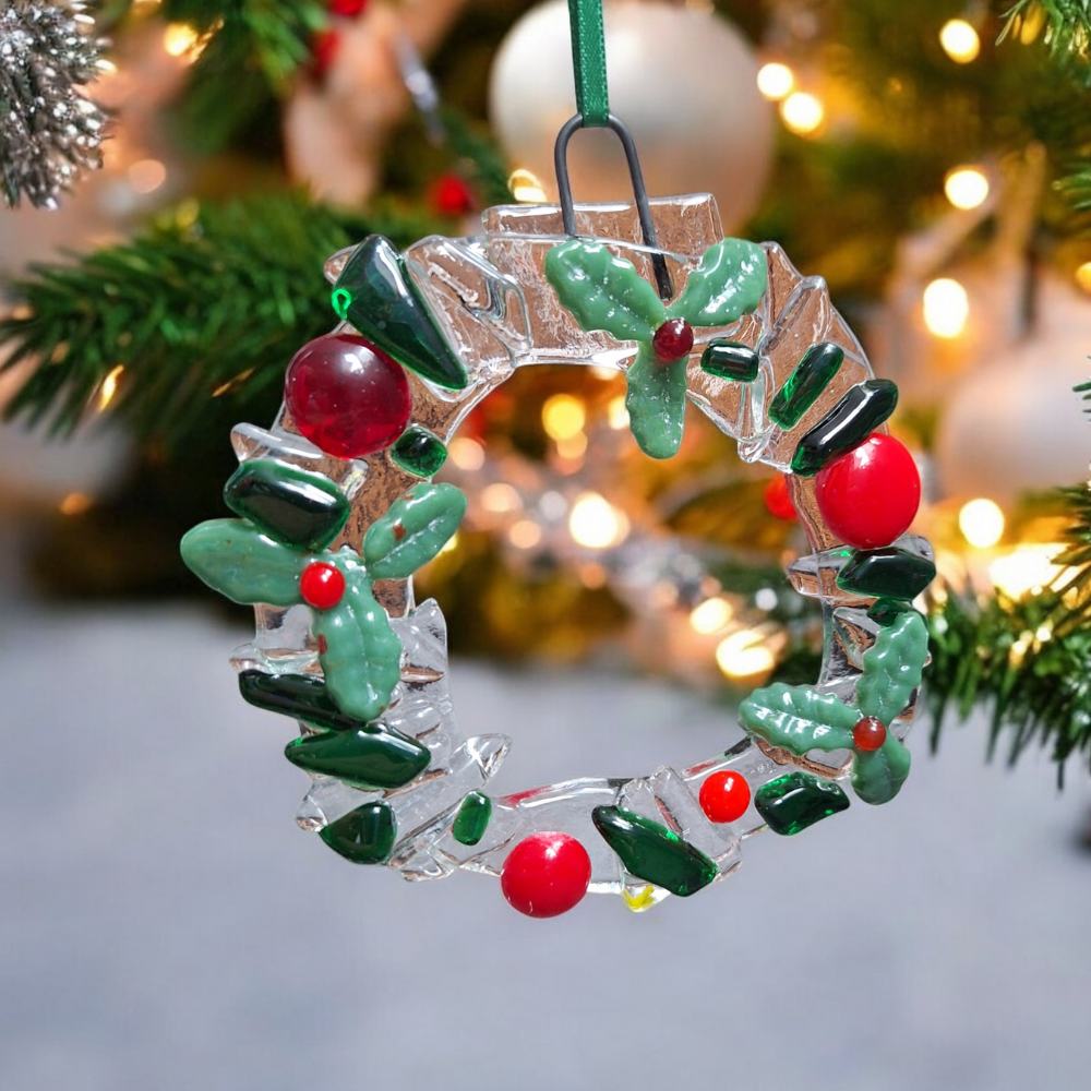 Handmade fused glass Christmas wreath ornament with holly leaves and red berries hanging on a tree