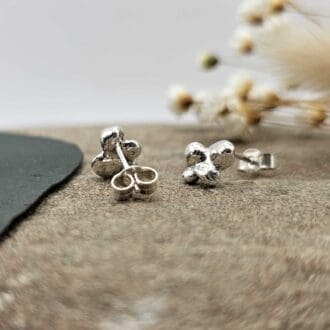 Pair of handcrafted recycled sterling silver cluster bead stud earrings displayed hanging on decorative stone