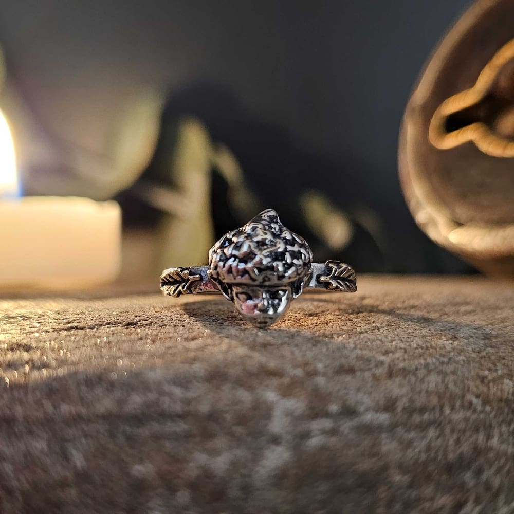 Handcrafted recycled oxidised sterling silver autumnal elf with acorn hat ring displayed on decorative stone by candlelight