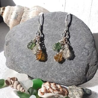 tri-colour sea glass dangly earrings with silver hooks and wrapped in silver wire displayed on a grey pebble