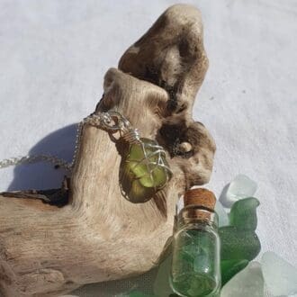 A silver wire wrapped piece of sea glass hanging on a silver chain displayed on a piece of driftwood