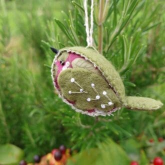 a hand stitched felt and fabric bird in olive green and a green and mauve fabric with pearly snowberries