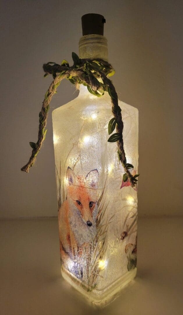 Lit up Square glass gin bottle with fox detailing. Leafy jute twine tied around the neck of the bottle