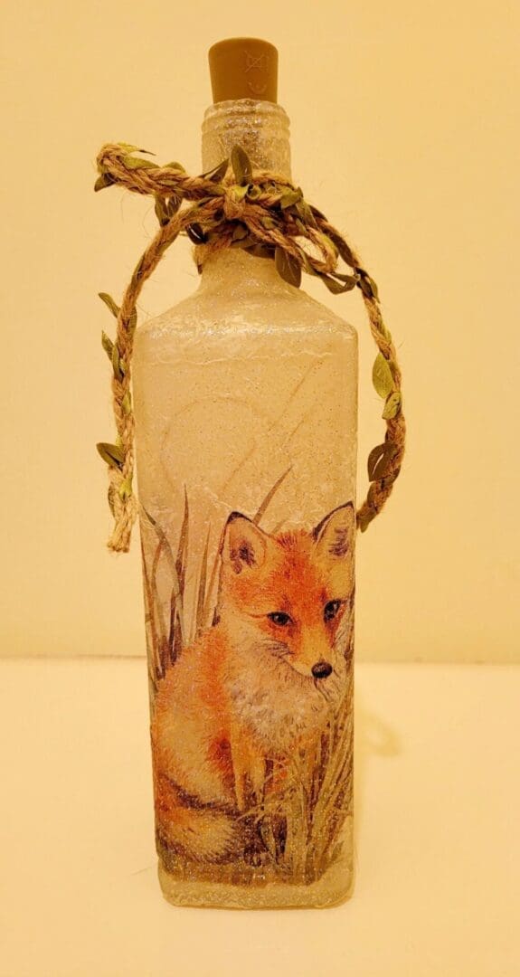 Square glass gin bottle with fox detailing. Leafy jute twine tied around the neck of the bottle