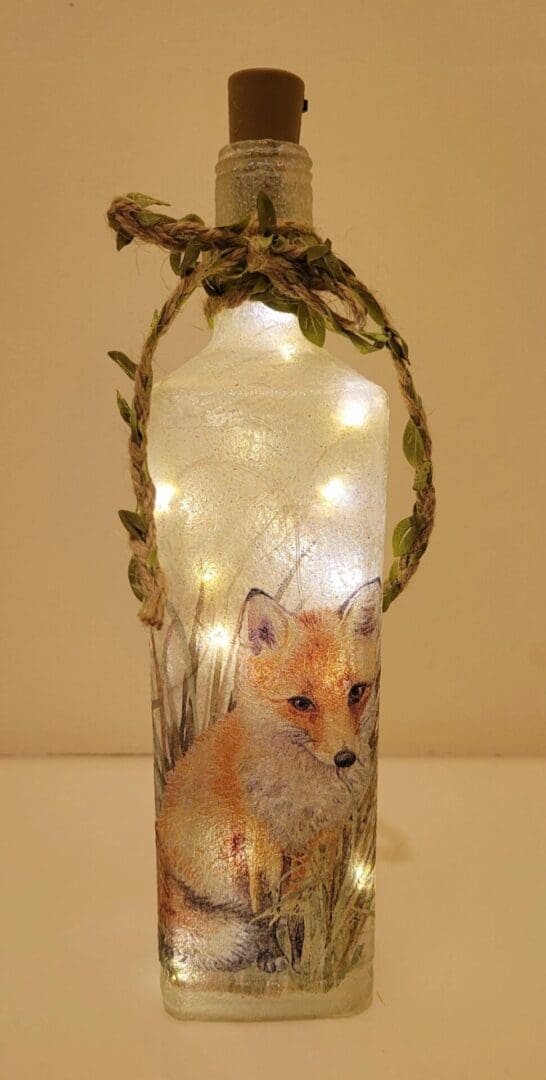 Lit up Square glass gin bottle with fox detailing. Leafy jute twine tied around the neck of the bottle