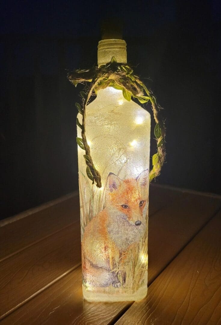 Lit up Square glass gin bottle with fox detailing. Leafy jute twine tied around the neck of the bottle