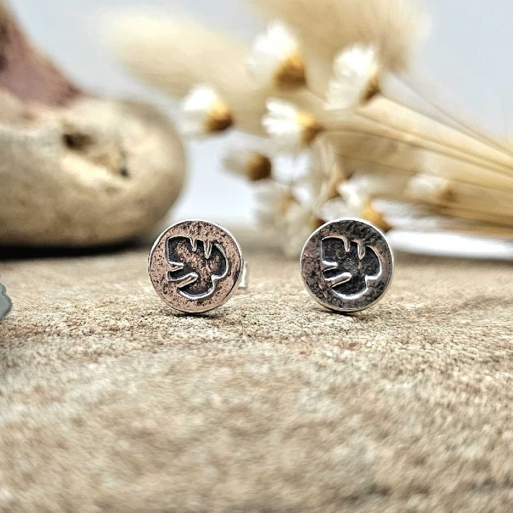 Handcrafted recycled sterling silver monster leaf print round stud earrings displayed on decorative sand coloured stone