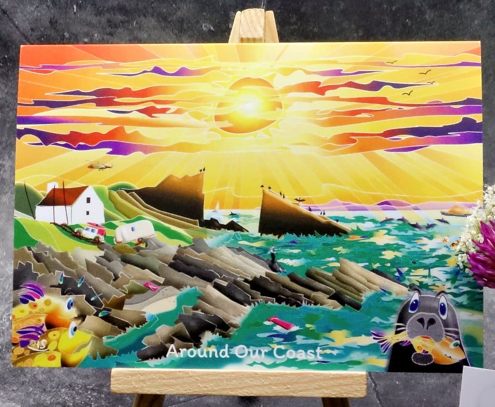 Larger image titled Around Our Coast showing an A6 size greetings card, blank inside, on a small easel. A gently humorous bright and sunny coastal scene of Split Rock in Assynt, holiday mishaps and animal misadventure.