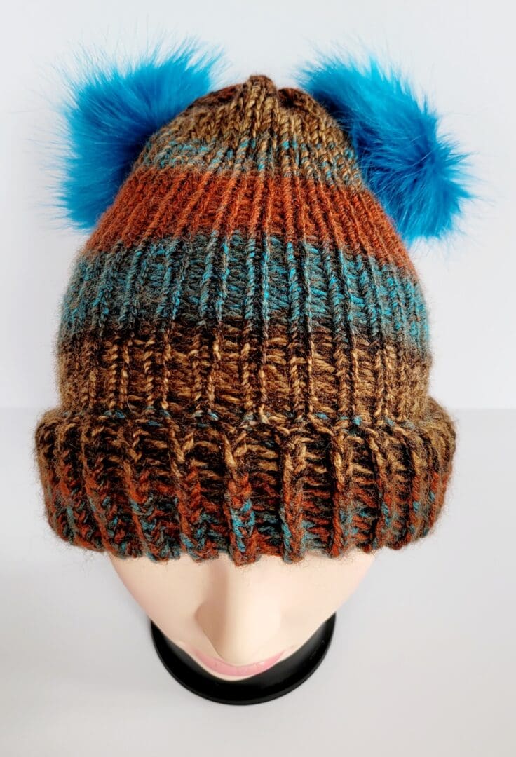 Brown and blue striped hat with brim featuring two blue fluffy pom poms