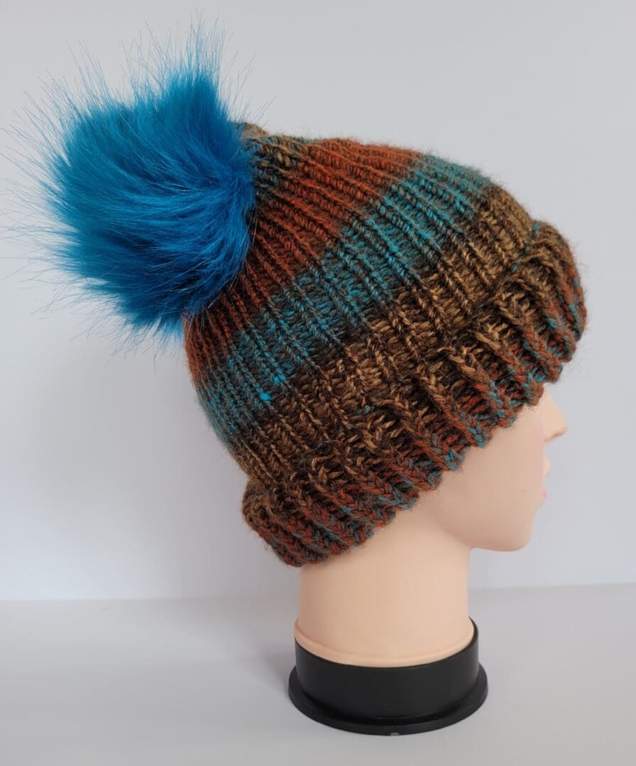 Brown and blue striped hat with brim featuring two blue fluffy pom poms