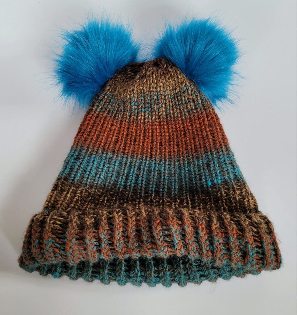 Brown and blue striped hat with brim featuring two blue fluffy pom poms