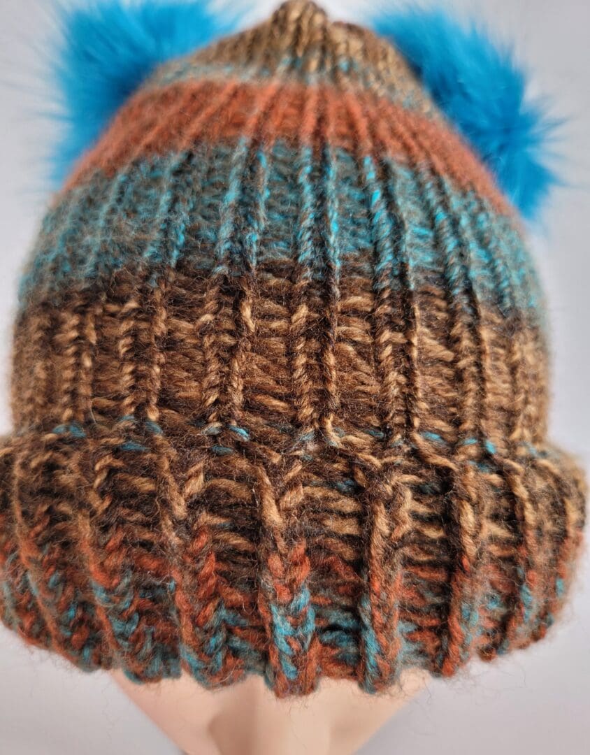 Brown and blue striped hat with brim featuring two blue fluffy pom poms