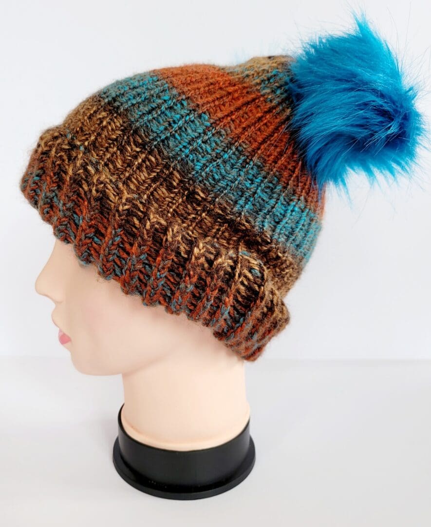 Brown and blue striped hat with brim featuring two blue fluffy pom poms