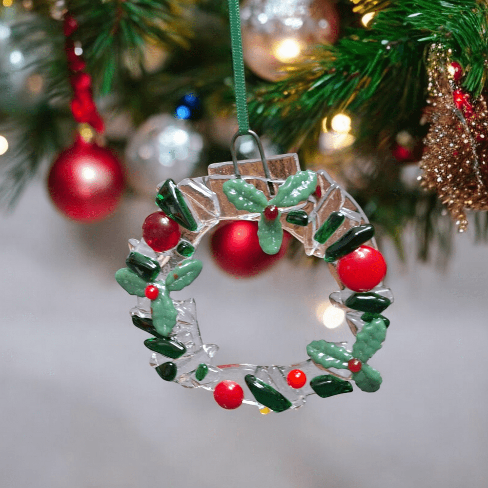 Handmade fused glass Christmas wreath ornament with holly leaves and red berries hanging on a tree