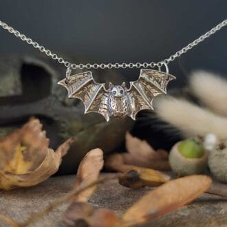 Handcrafted recycled sterling silver gothic vampire bat pendant hanging on chain displayed above autumnal setting