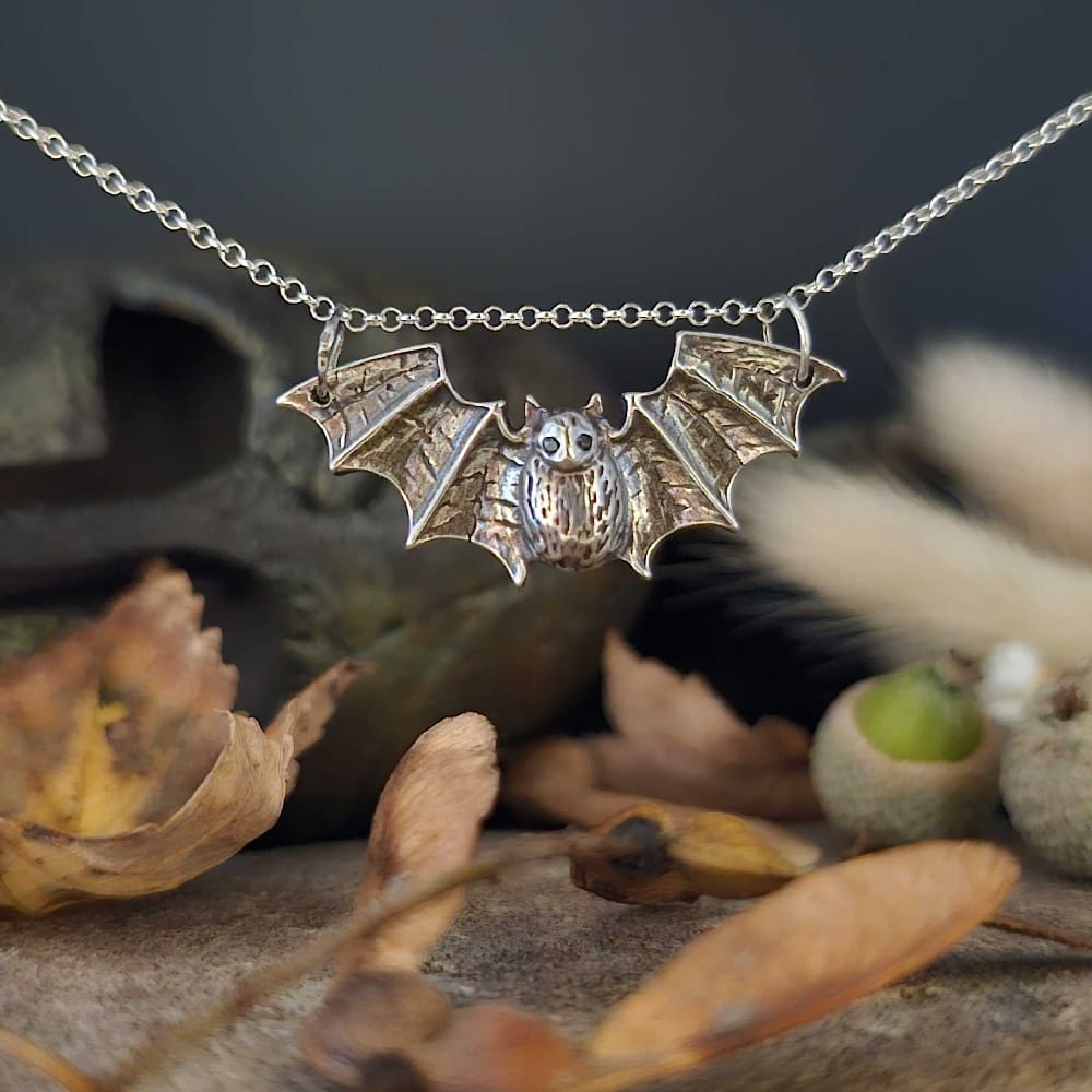 Handcrafted recycled sterling silver gothic vampire bat pendant hanging on chain displayed above autumnal setting