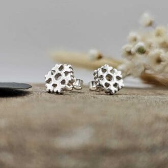 Pair of handcrafted recycled polished sterling silver winter snowflake stud earrings displayed on decorative stone