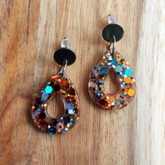 Small teardrop earrings, made in clear resin with a turquoise and copper chunky glitter mix added. They are fixed onto small flat silver tone stud tops, and displayed on a wooden board.