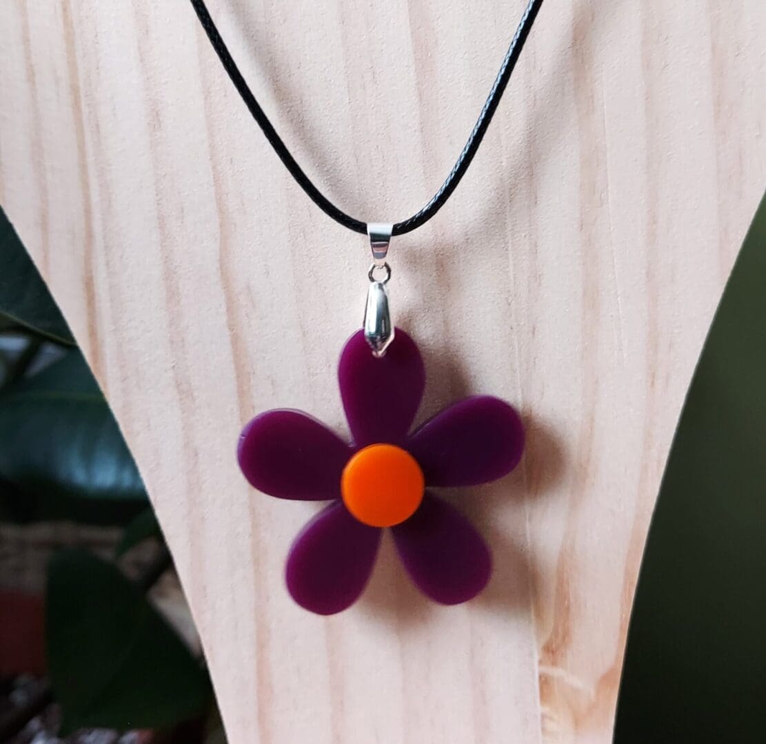 Purple and orange daisy pendant handmade in resin and fixed onto a black cord necklace.