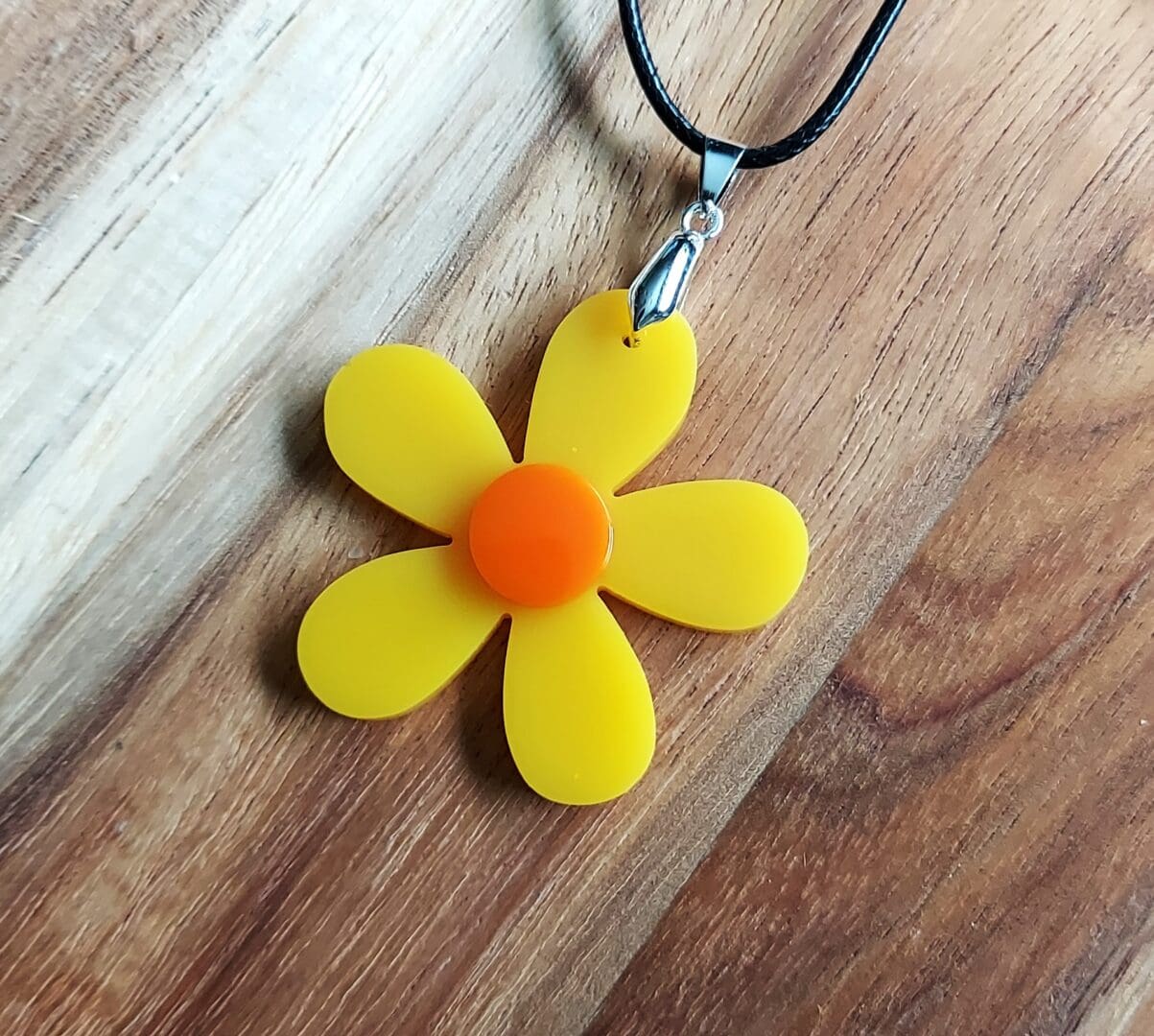 Retro Yellow daisy pendant with an orange centre, and hung from a black cord necklace.