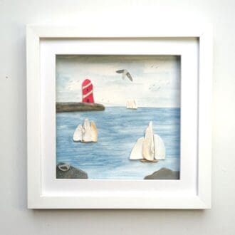 framed picture of three sailing boats and a red and white lighthouse made from beachcombed finds including sea shells and sea pottery