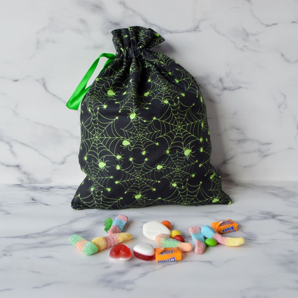 Black halloween trick or treat bag with green spiders and cobwebs. The bag has a drawstring closure with a green ribbon