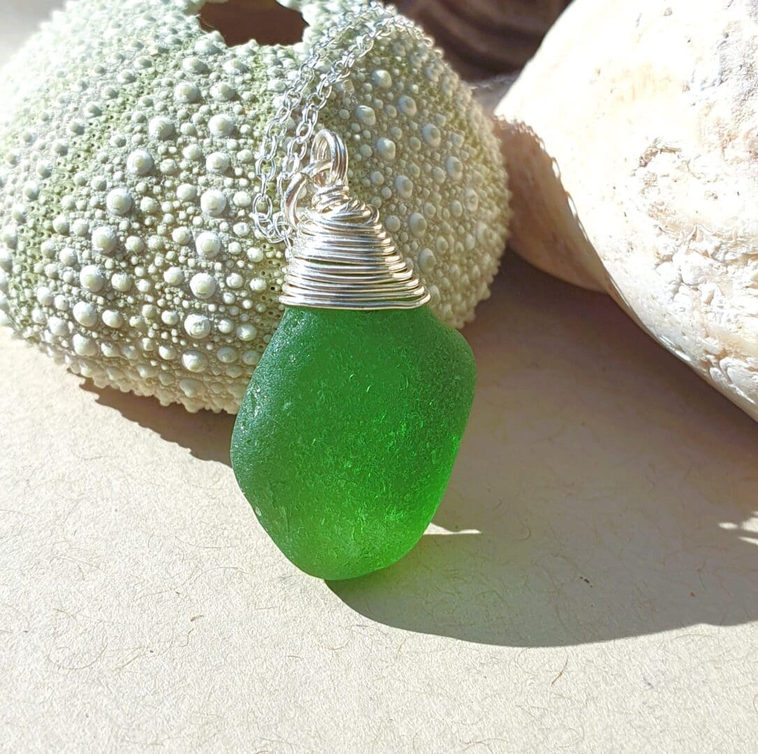 A bright green sea glass pendant leaning against a small sea urchin with a small bit of shell to the right of the shot