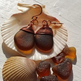 A pair of dark amber, copper wire and rose gold drop earrings displayed inside a large cockle shell